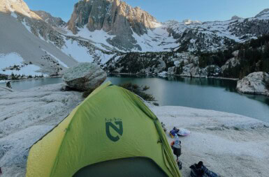 Neon green tent in foreground with beautiful mountains and a lake in the background